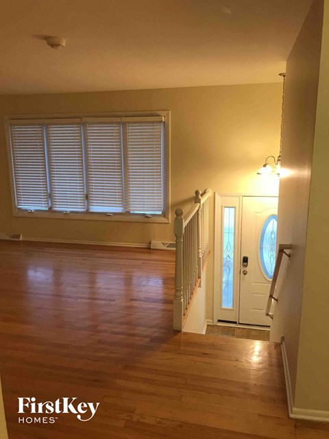 A wooden floor in a house with a white door and a window with blinds.