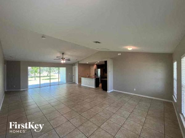 an empty living room with tile flooring and a kitchen