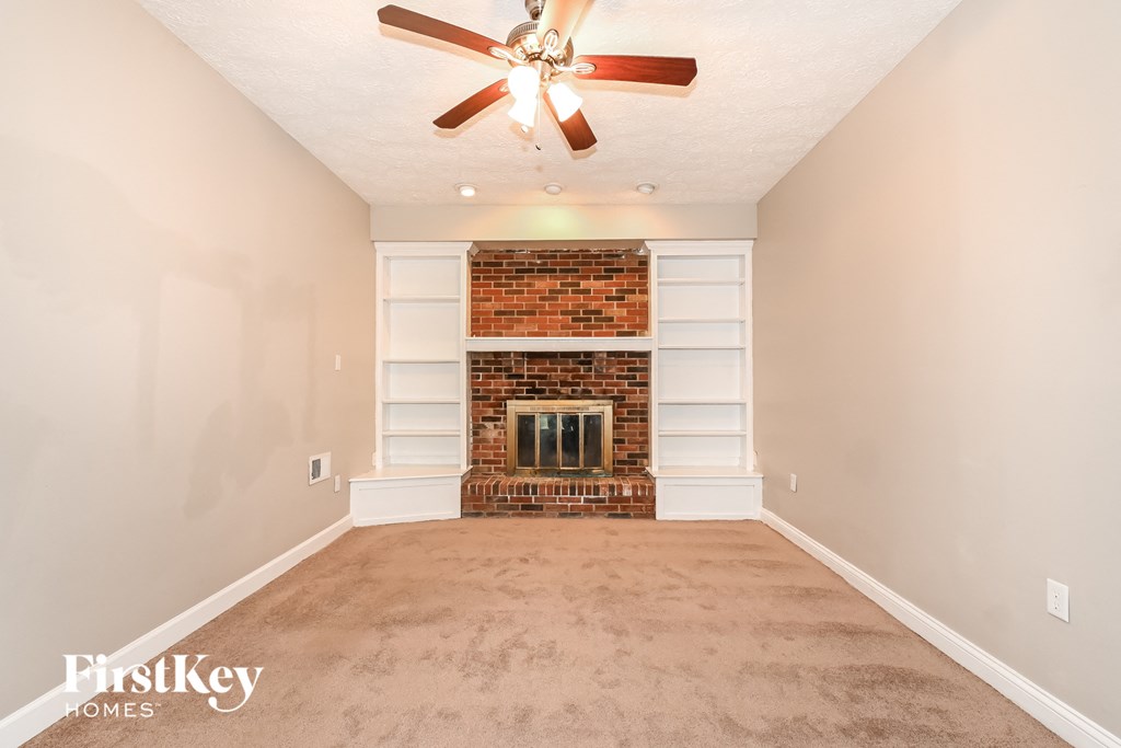 a empty living room with a brick fireplace and a ceiling fan