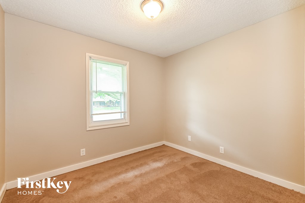 the spacious bedroom with carpeted flooring and a window