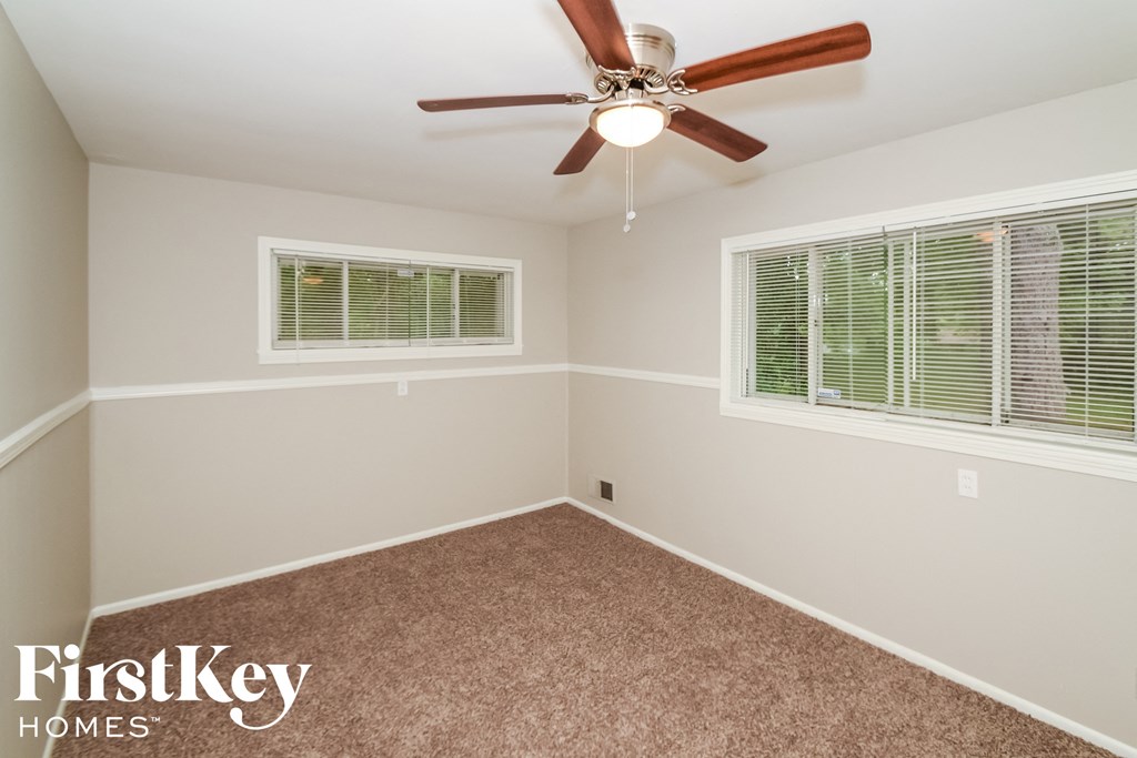 an empty room with a ceiling fan and two windows