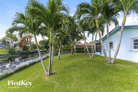 A white house with a blue roof is surrounded by palm trees.