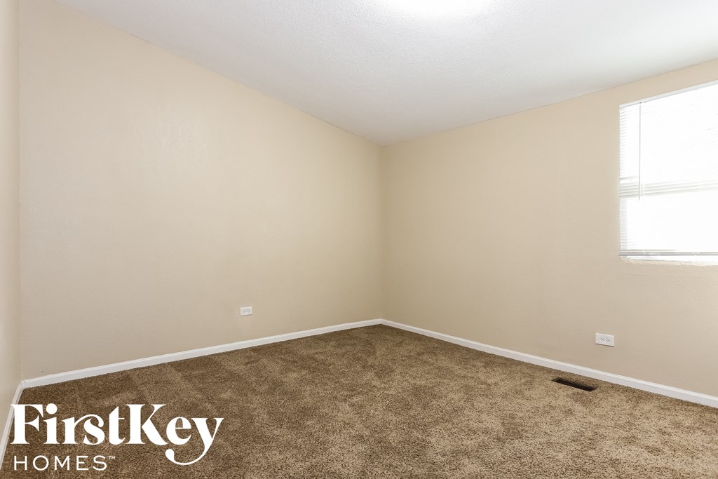 the bedroom of a small house with carpet and two windows