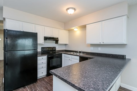 A black refrigerator is in a kitchen with white cabinets.