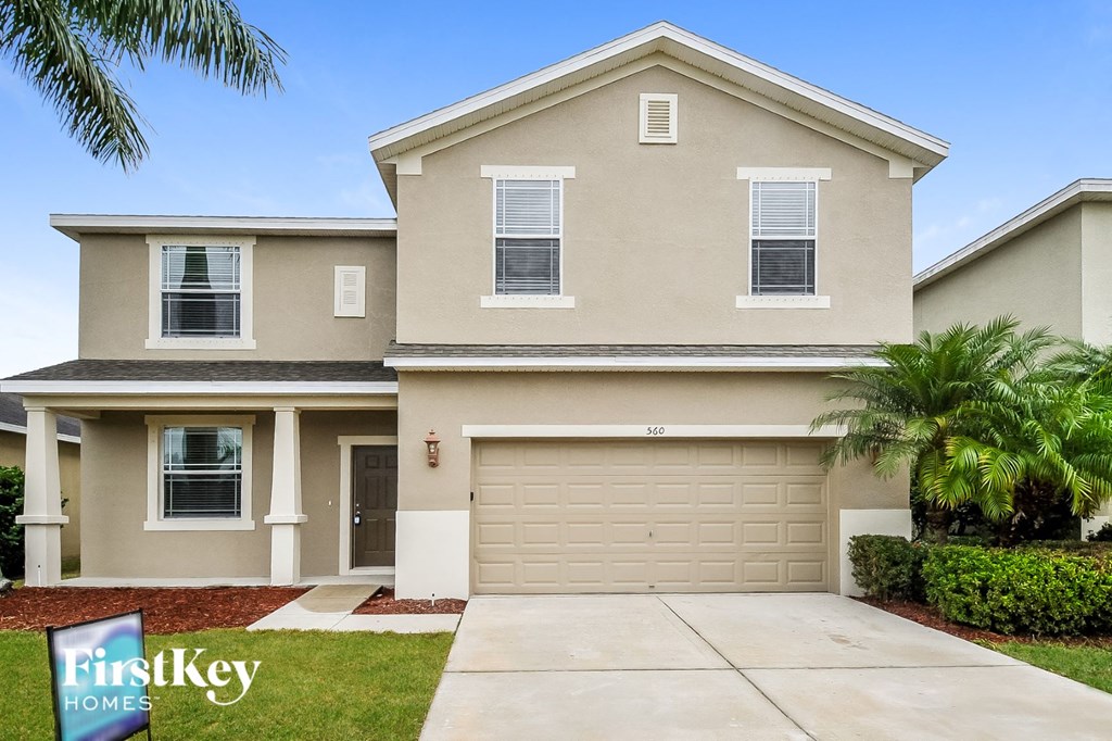 a beige house with a garage door and palm trees