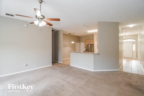 an empty living room with a ceiling fan and a kitchen