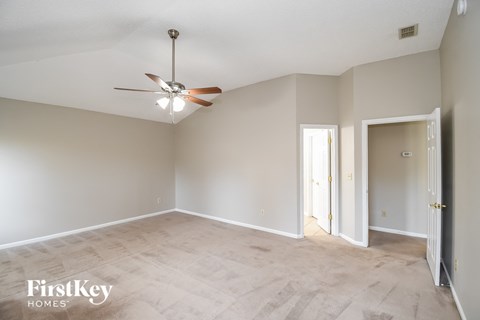 an empty living room with a ceiling fan and a door to a hallway