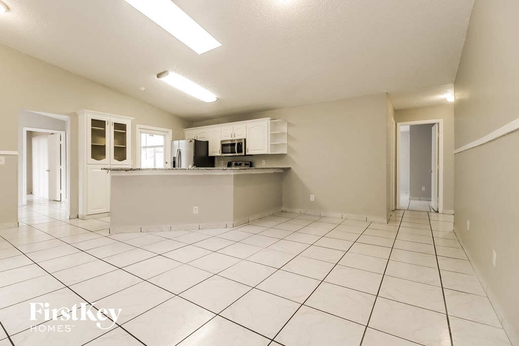 A spacious kitchen with white tile flooring and a large island in the middle.