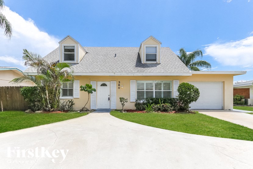 A house with a white door and windows is surrounded by greenery.