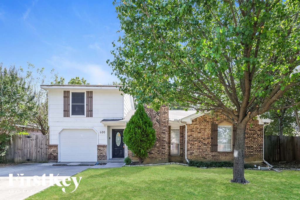 A white house with a black door and windows is surrounded by a green lawn and trees.