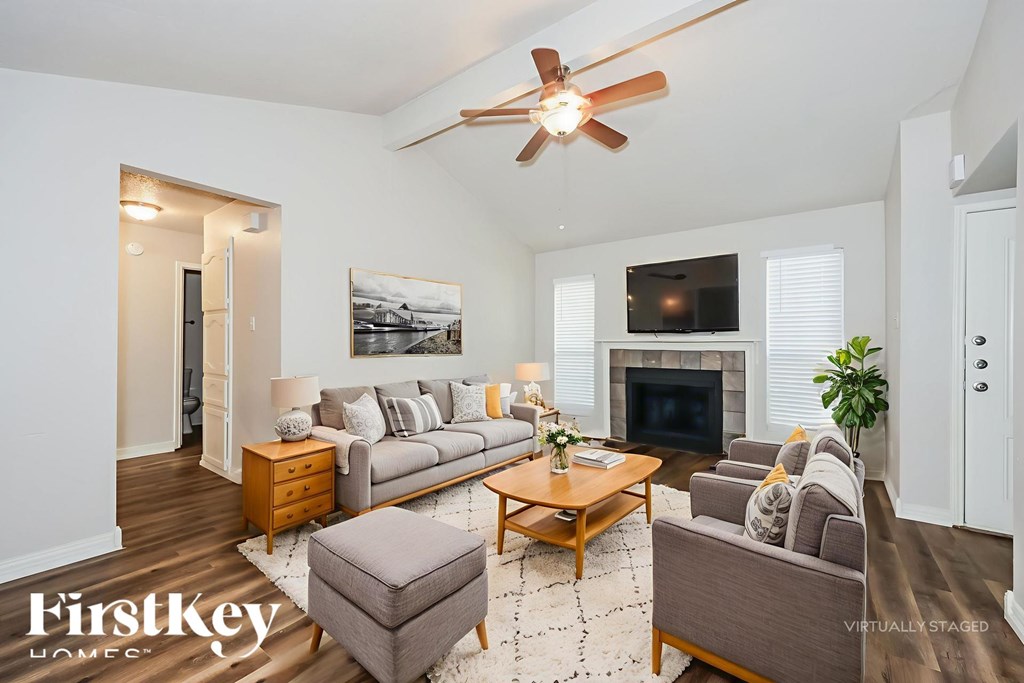 A living room with a grey couch, a coffee table, a fireplace, and a ceiling fan.
