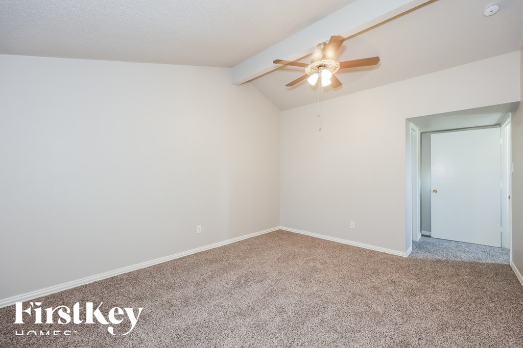 A carpeted room with a ceiling fan and a door.
