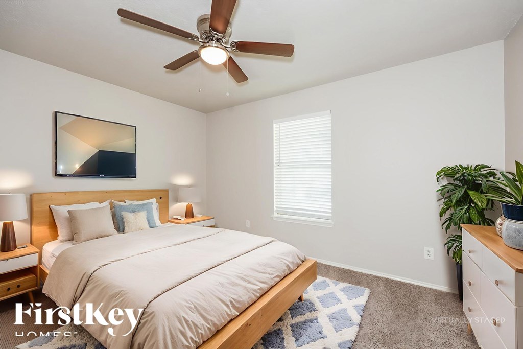 A bedroom with a bed, a ceiling fan, and a painting on the wall.