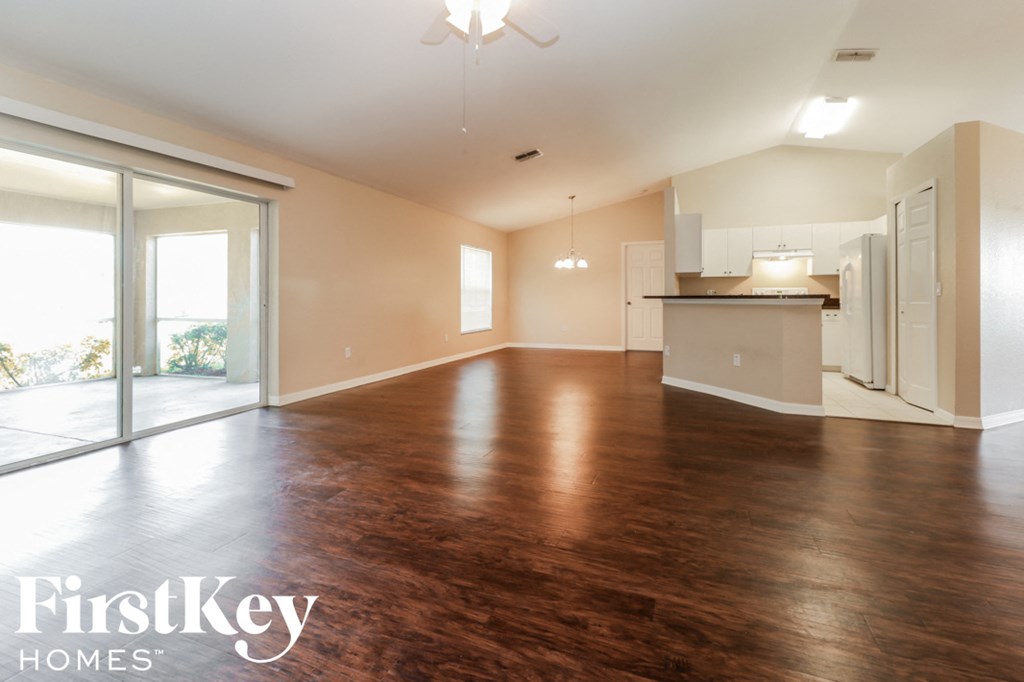 A spacious room with wooden flooring and a kitchen area in the background.