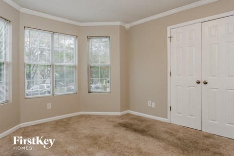 A room with a carpeted floor, two windows with blinds, and a white door.