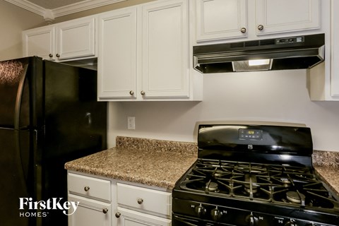 A black stove top oven sits on a granite countertop in a kitchen with white cabinets.
