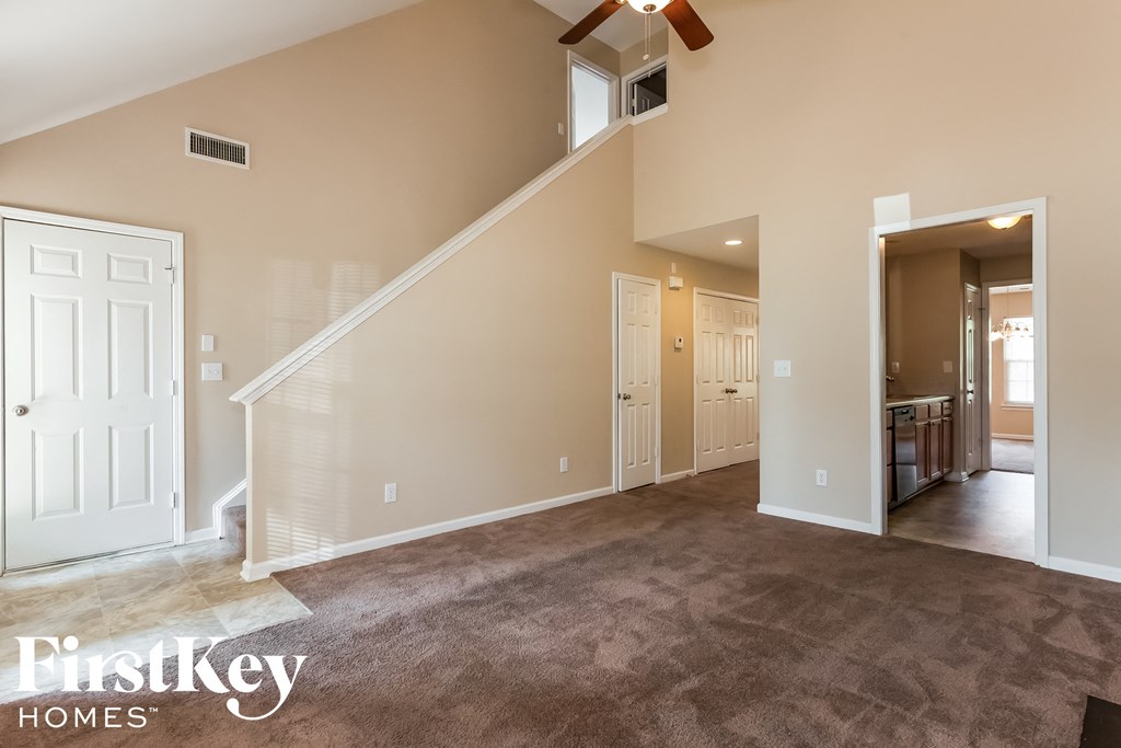 A spacious living room with a staircase and a ceiling fan.