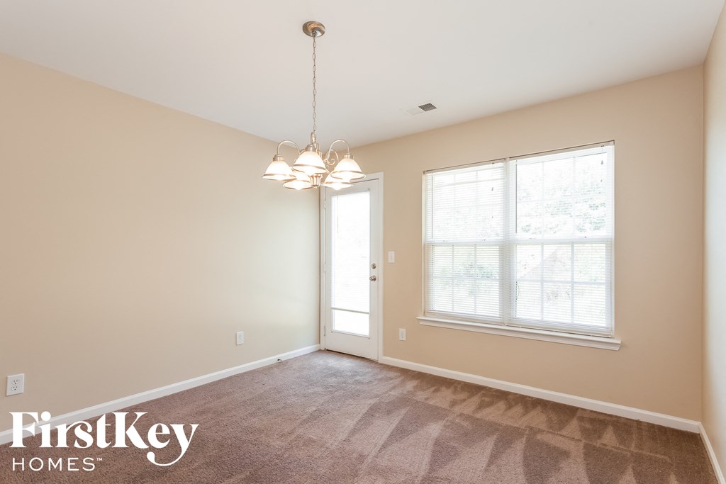 A room with a carpet floor, a door, a window, and a chandelier.