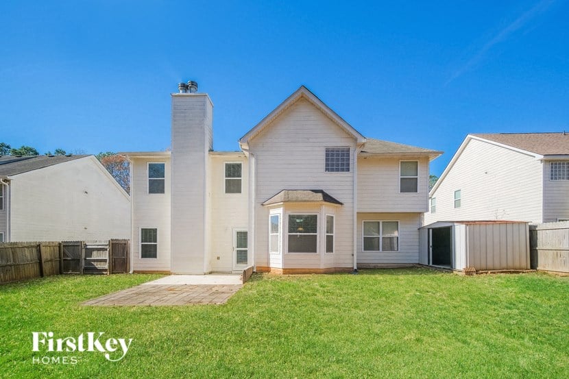 the backyard of a white house with a green lawn and a fence