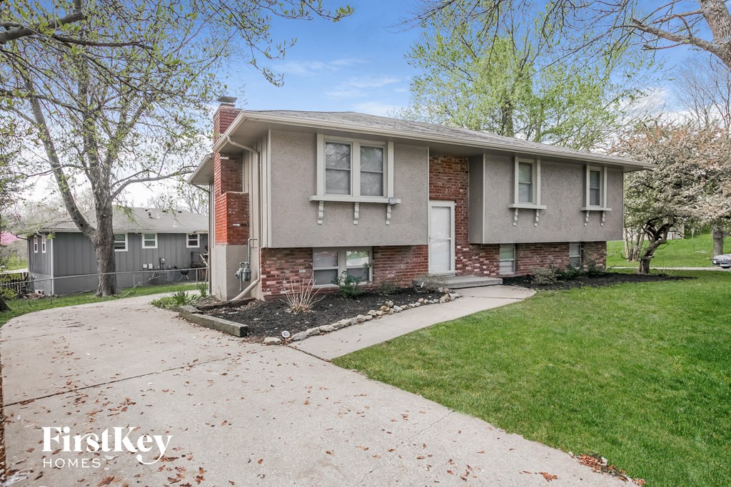 a small gray house with a driveway and a lawn