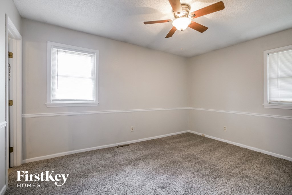 the living room of an empty home with a ceiling fan and two windows