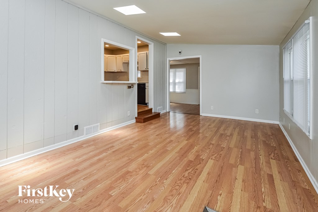A room with wooden flooring and white walls, with a doorway leading to another room.