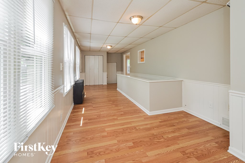 A room with wooden floors and white walls, with a window on the left side.