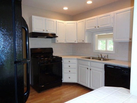 A black refrigerator is in a kitchen with white cabinets.