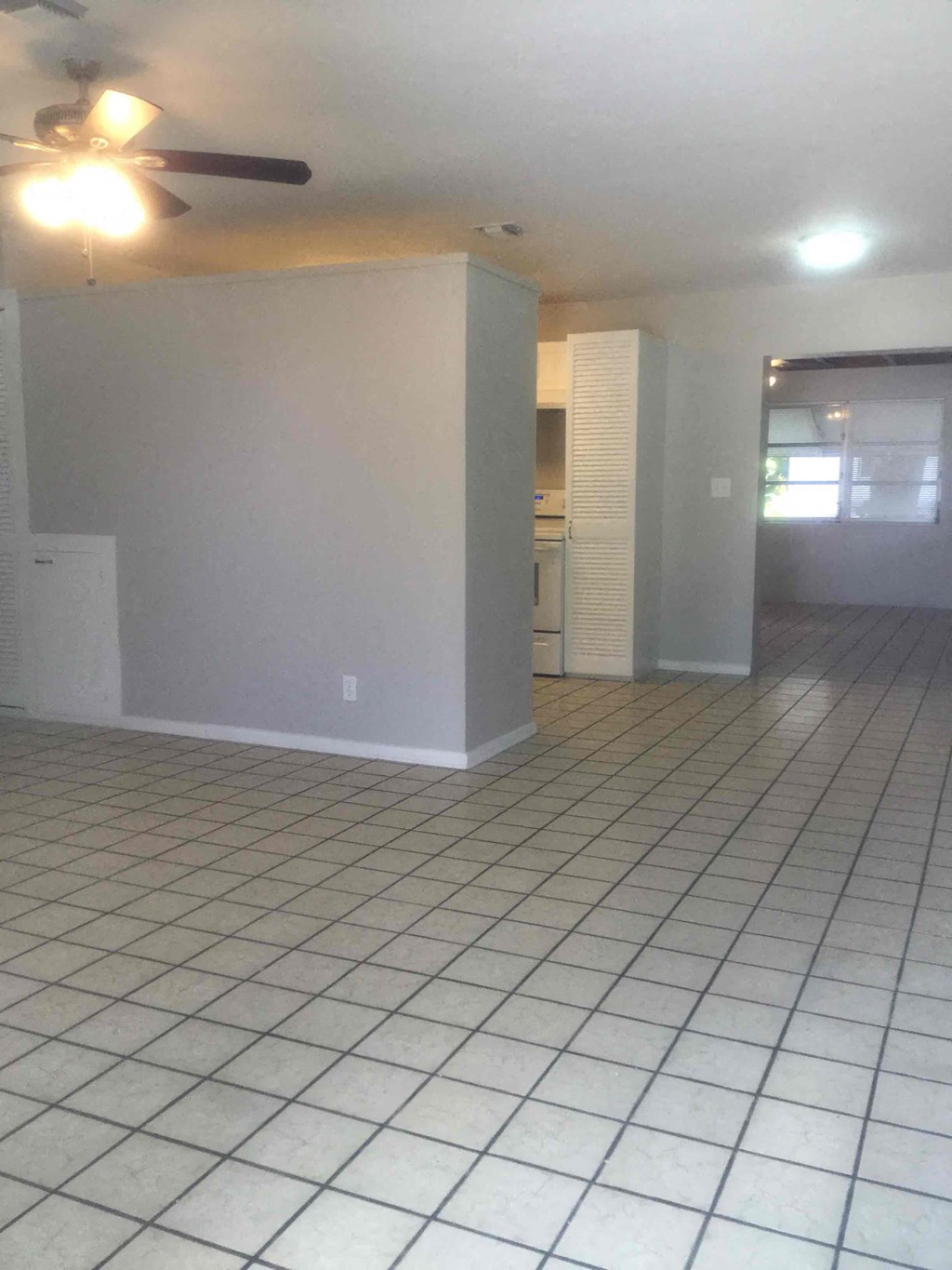 an empty living room with a tile floor and a ceiling fan
