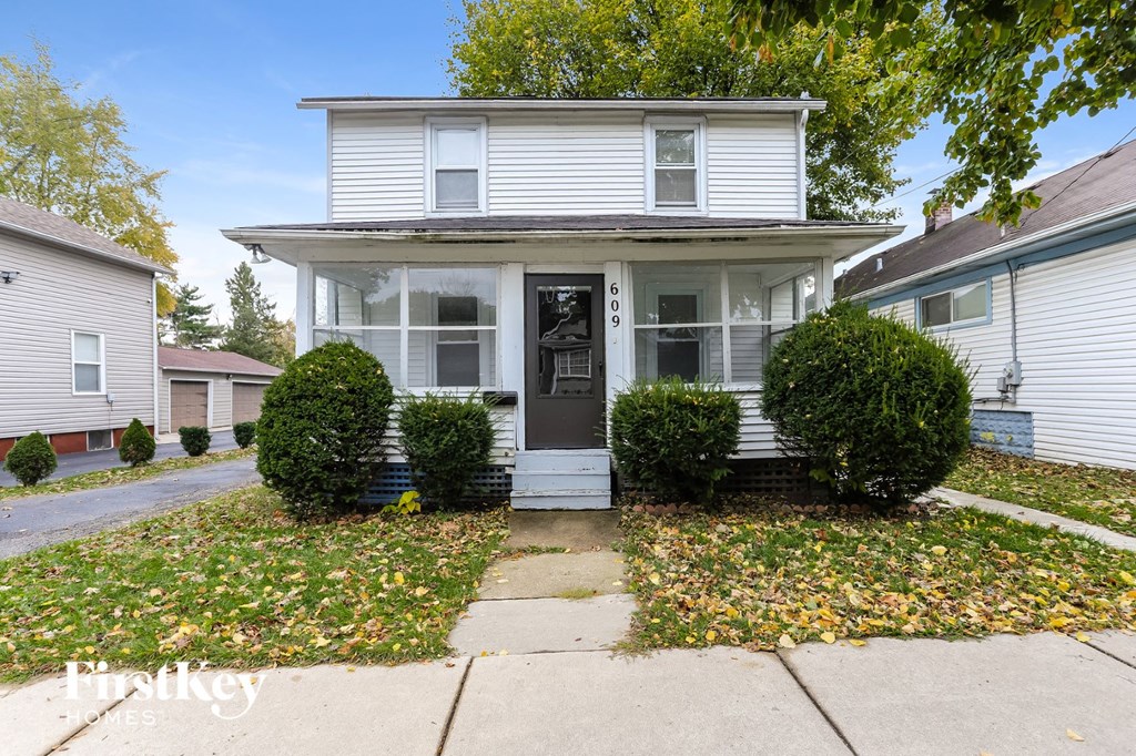 A white house with a black front door and two bushes on either side.