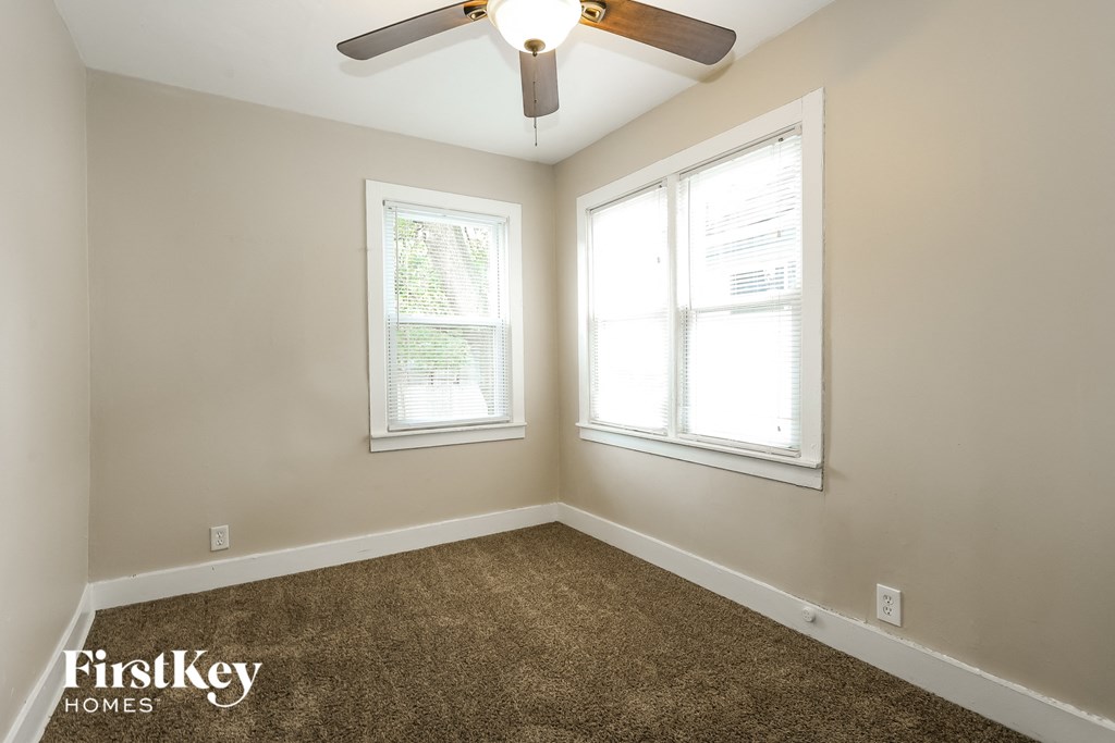 A room with a carpet floor, a ceiling fan, and two windows.
