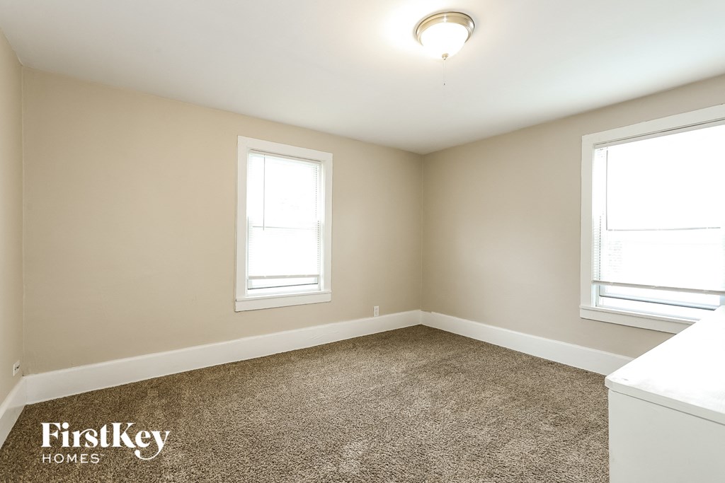 A room with a carpeted floor and two windows.