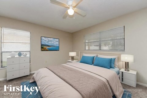 A bedroom with a large bed, a ceiling fan, and a painting on the wall.