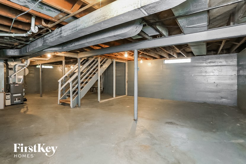 A spacious basement with a staircase and a pipe running along the wall.