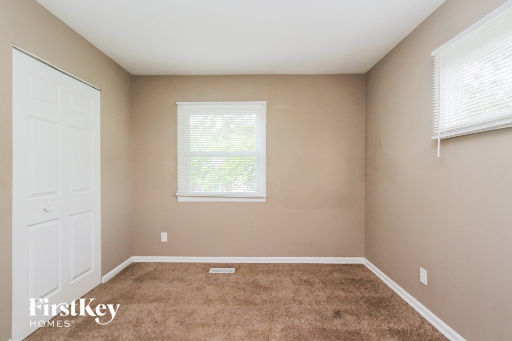 a carpeted room with a white door and two windows