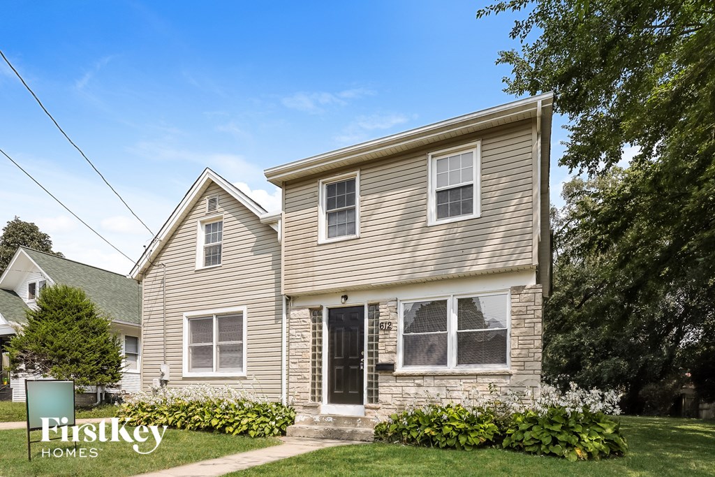 a single story house with tan siding and a sidewalk in front of a yard