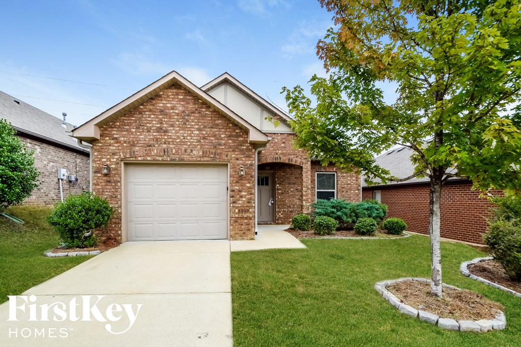 A brick house with a garage door and a tree in front.