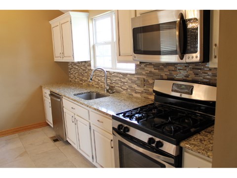 A kitchen with a black microwave above a stove and a sink with a granite countertop.