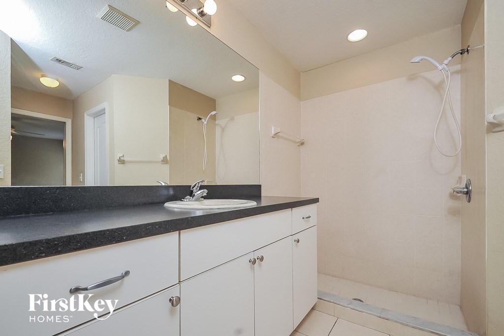 a bathroom with white cabinets and a sink and a shower
