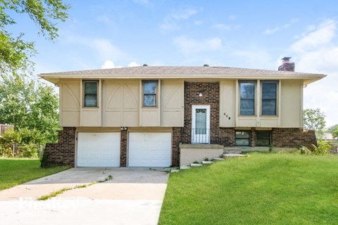 a tan house with two garage doors and a lawn