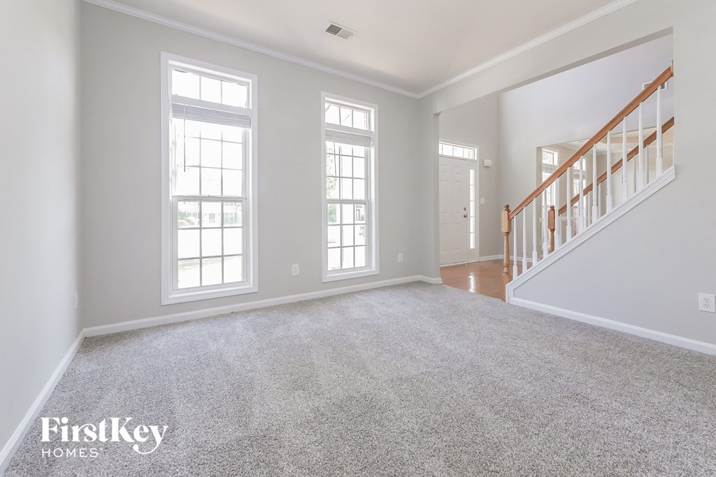 A spacious room with a carpeted floor, two windows, and a staircase.