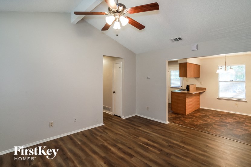 an empty living room with a ceiling fan and a kitchen