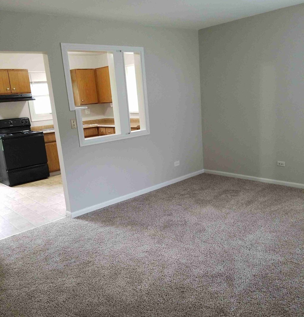 an empty living room with a window and a kitchen