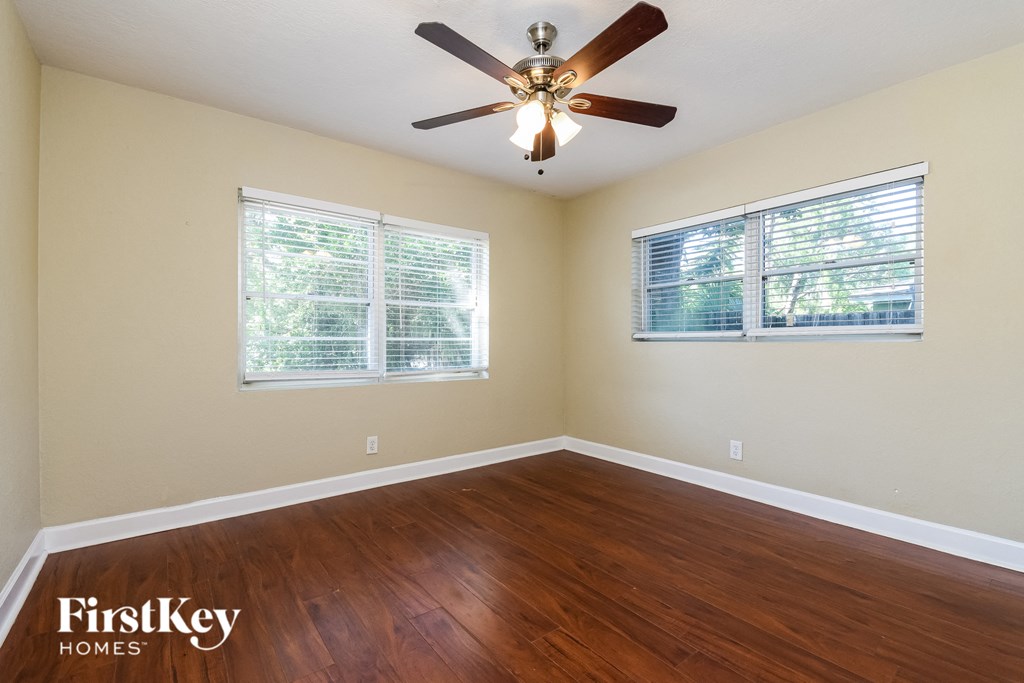 A room with a ceiling fan and two windows.
