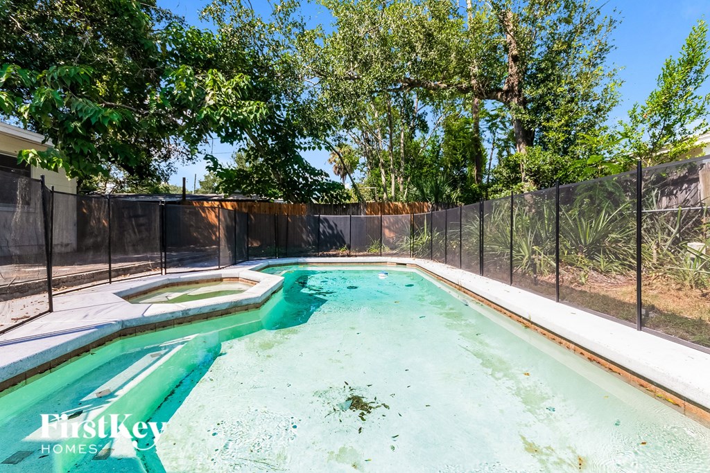 A pool surrounded by a black fence and trees.
