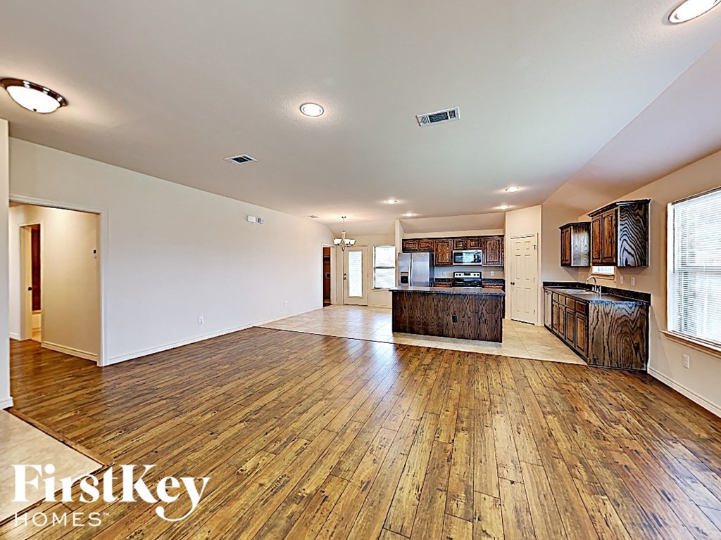 A spacious room with wooden floors and a kitchen area with a refrigerator, cabinets, and a counter.