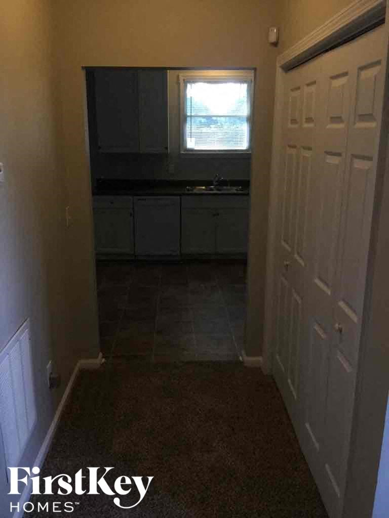 A hallway with a white door and a window in the kitchen.