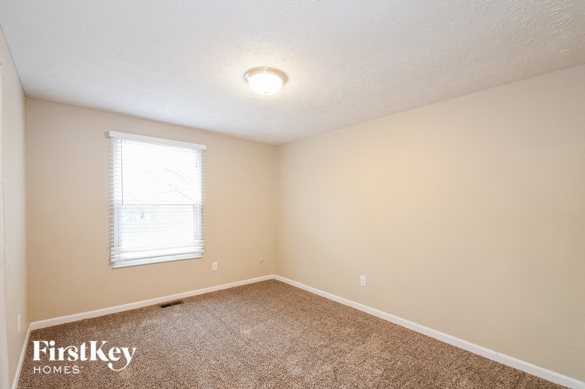 the bedroom of a house with carpet and a window