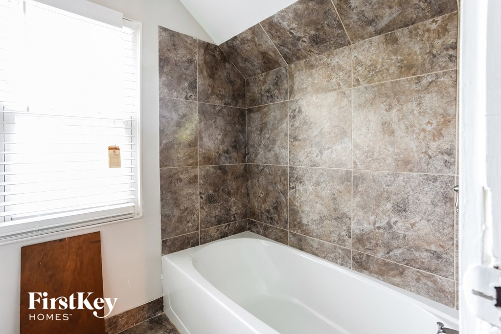 a tiled bathroom with a white bath tub and a window
