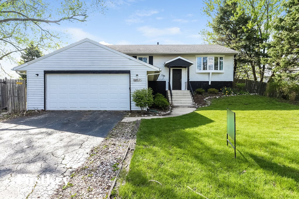 A white house with a garage and a green sign in front.
